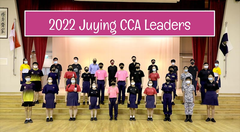 Group of masked students and teachers posing indoors under a pink banner reading 2022 Juying CCA Leaders.